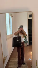 Tote bag de ecocuero color marrón oscuro con textura de cocodrilo, detalles de tachas en los laterales y asas de cuero marrón liso. Incluye un dije de guampa blanca colgando.