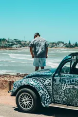 Remerón de manga corta, corte holgado, color gris lavado, con estampado frontal de una escena de playa con palmeras y texto.