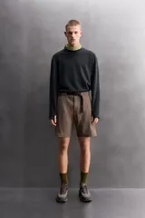 Bermuda de ajuste regular color marrón oscuro, confeccionada en tejido técnico compacto con elasticidad. Presenta cintura ajustable con cinturón negro a contraste, bolsillos frontales y un bolsillo cargo con cierre de cremallera oculta en la pernera.