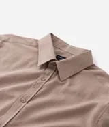 Camisa de manga larga con cuello inglés y cierre frontal de botones, confeccionada en tricolina de algodón color beige.