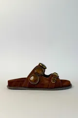 Sandalias planas de gamuza marrón, con dos tiras anchas adornadas con grandes piedras redondas facetadas en tonos marrones con bordes metálicos dorados.