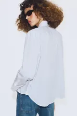 Camisa de algodón con estampado de rayas verticales, cuello solapa y puños en color blanco a contraste. Presenta cierre frontal con botones, bolsillo de plastrón en el delantero y bajo asimétrico.