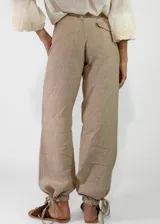 Pantalón de lino color beige, de corte holgado tipo jogger con puños ajustables con cintas en los tobillos, bolsillos laterales y cierre frontal con botón y cremallera.