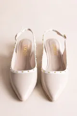 Chatitas destalonadas de cuero charolado color beige con punta fina, taco bajo y detalle de tachas metálicas doradas alrededor del borde.