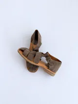 Sandalias cangrejeras de gamuza color marrón, con punta redonda, taco bajo, talonera cerrada y tira con hebilla metálica ajustable en el tobillo.