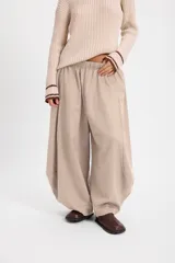 Pantalon de corte balloon, color crudo, con silueta holgada y cortes laterales circulares. Presenta cintura elástica con cordón ajustable.