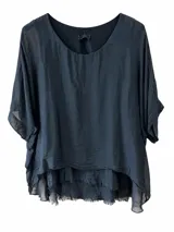 Blusa de seda color negro, de diseño amplio y holgado, con cuello redondo y mangas cortas. Presenta dobladillo asimétrico en capas con terminaciones deshilachadas.