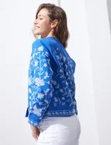 Chaqueta de algodón bordada, color azul con bordado floral blanco, con cuello a la base y escote en V, abertura central con botón.