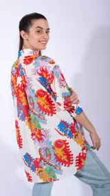 Camisa blanca de manga larga con estampado abstracto en colores rojo, naranja y azul. Tiene cuello clásico y cierre frontal de botones.