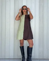 Vestido corto de diseño bicolor con paneles verticales en verde claro y marrón oscuro. Presenta un escote recto, corte sin mangas y una textura arrugada en la tela. Incluye bolsillos laterales ocultos y cierre en la espalda.