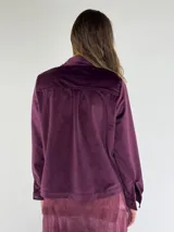 Chaqueta azul marino de terciopelo con cuello camisero, cierre frontal con botones, dos bolsillos de parche con solapa y mangas largas con puños abotonados.