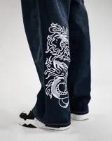 Pantalón jean azul oscuro, corte baggy, tiro medio y estampado con serigrafía de dragón, texto y símbolos.
