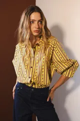 Camisa de manga larga con cuello clásico y cierre frontal de botones. Presenta un diseño de rayas verticales verdes y blancas con un estampado lineal de pequeñas flores rojas.