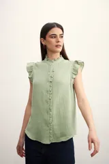 Camisa color amarillo pálido con textura arrugada, cuello mao con volados, cierre frontal con botones y mangas cortas con volados.