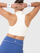 Conjunto deportivo compuesto por un top corto tipo polo sin mangas en color blanco y una pollera deportiva azul con cintura alta y detalle de vivo en contraste.