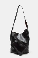 Bolso de hombro tipo saca asimétrica, color negro, con acabado de piel brillante. Posee un asa de hombro ajustable y cierre magnético. Incluye una cartera interior extraíble.