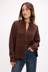 Cárdigan de tejido calado color blanco, con cierre frontal completo, cuello alto y mangas largas. Presenta un diseño con patrón de perforaciones geométricas y ajuste relajado.