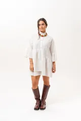 Vestido corto de broderie color crudo, con cuello camisero, cierre frontal parcial con botones, mangas tres cuartos acampanadas y corte evasé con volados.