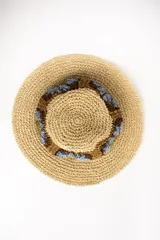 Sombrero de ala ancha color tostado, tejido en papel con detalles de apliques de crochet en la parte central con diseño de flores en tonos celestes, marrones y verde oliva.