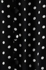 Vestido midi negro con estampado de lunares blancos, escote en V pronunciado, botones forrados frontales y mangas largas abullonadas con puños elásticos.