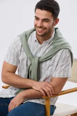 Camisa de manga corta confeccionada en mezcla de lino y algodón, con diseño a cuadros en tonos gris, blanco y azul. Presenta cuello camisero con botones y bolsillo ojal en el pecho con detalle bordado.