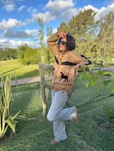 Cardigan de lana color camel con cuello polo, botones frontales y detalles de caballos hechos a mano en cuero negro. Presenta una franja horizontal negra tejida en el pecho y en las mangas.