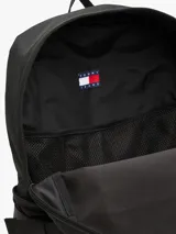 Mochila estilo retro de la marca Tommy Jeans, color negro, inspirada en modelos utilitarios. Cuenta con compartimento principal con cierre de cremallera, bolsillo exterior con cremallera, panel delantero con textura acolchada y parche con el logo de la marca en la parte superior. Incorpora correas ajustables, asa superior y detalles de tiras trenzadas.