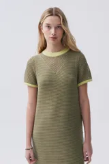 Vestido largo verde de tejido de punto calado, con escote redondo y mangas cortas. Tiene tajos laterales y ribetes en color amarillo.