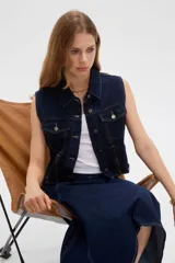 Chaleco de denim azul oscuro con bolsillos con solapa en el pecho, cierres decorativos y cierre frontal con botones metálicos.