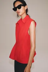 Camisa de cuello solapa y manga sisa, de color blanco. Presenta bajo acabado en peplum y cierre frontal con botones ocultos.