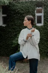 Camisa de corte oversize color crudo, con cuello mao y puños con detalle de volados en color azul. Presenta cierre frontal con botones forrados y mangas largas abullonadas.