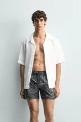 Bañador de hombre de tejido técnico, color gris oscuro con estampado abstracto en tonos más claros. Presenta cintura elástica ajustable con cordón, bolsillos laterales y un bolsillo trasero de plastrón.