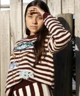 Sweater artesanal de punto tejido a mano en 100% lana merino, con diseño de rayas horizontales en color bordó y crudo, y detalle de diseño floral bordado en la parte frontal.