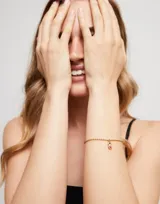 Pulsera dorada con cadena de bolitas y cierre de mosquetón. Incluye un dije circular con el logo de la marca.