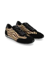 Sneaker de mujer con diseño de animal print tipo cebra en tonos marrón y negro, combinada con paneles de gamuza negra en la puntera, talón y laterales. Presenta cordones negros y una suela plana de perfil bajo.