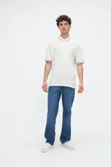 Remera polo manga corta color blanco, confeccionada en tela piqué de algodón lavado con textura extra suave. Cuenta con media cartera de botones, cuello y puños acanalados con diseño de líneas a contratono, y bordado sutil de la marca en el pecho. Calce clásico.