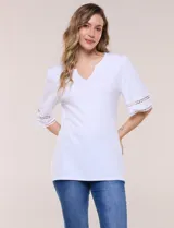 Remera blanca de silueta recta y algodón suave, con escote redondo y pequeña abertura central tipo gota. Presenta mangas de largo intermedio con aplicación horizontal de puntilla calada al tono y ruedo recto con tajos laterales.
