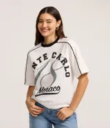Remera blanca de algodón con cuello redondo y ribete negro. Presenta un estampado grande con el texto "MONTE CARLO" y "Monaco" en tonos negro y gris, con un diseño que simula un número 8 o un símbolo de infinito.