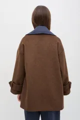 Tapado de paño de lana color marrón con silueta oversize y hombros caídos. Presenta doble abotonadura frontal, solapas amplias con detalle en contraste azul, y mangas con ajuste en los puños.
