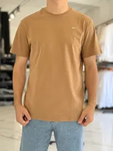Remera marrón tostado de corte clásico y mangas cortas, con cuello redondo y pequeño texto impreso en el pecho.