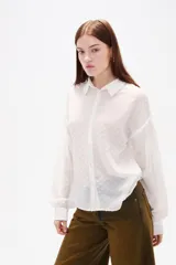 Camisa de color blanco con textura de pequeños puntos en relieve, cuello clásico, cierre frontal con botones y mangas largas con detalle de punto smock y puños elásticos.