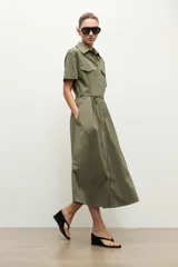 Maxi vestido camisero verde oliva, de manga corta, cuello camisero, cierre frontal con botones, bolsillos con solapa en el pecho, bolsillos laterales y lazo ajustable en la cintura.