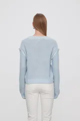 Sweater de punto color celeste, con diseño de trenzas frontales, cuello redondo y corte holgado.