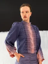 Chaqueta entallada de algodón tipo seda, teñida a mano con técnica tie-dye en tonos azul y naranja. Tiene cuello mao, mangas largas con puños abullonados y cierre frontal con broches.