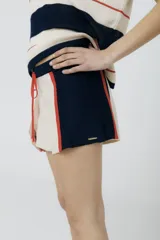 Short tejido en jersey color crudo con cintura elastizada azul marino y cordón de ajuste naranja. Presenta rayas verticales en los laterales con detalles de punto y terminaciones desflecadas.