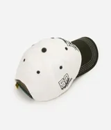 Gorra de béisbol de seis paneles, color blanco con visera curva en contraste de color verde militar. Presenta un bordado frontal de Snoopy junto a un banderín y el número cinco, y un bordado lateral con el texto 'Peanuts Athletic Department'.