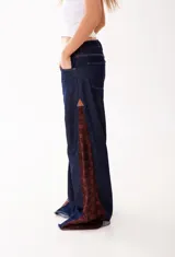 Pantalón de jean estilo wide leg en color azul oscuro, con paneles laterales de encaje en tono marrón rojizo. Presenta un corte amplio y estructura firme sin elasticidad.