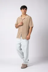 Camisa de punto calado en color beige, de manga corta y corte relajado. Presenta cuello tipo bowling, cierre frontal con botones al tono y una estructura liviana y respirable confeccionada en algodón.