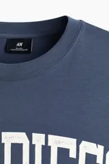Remera de algodón de peso medio, color azul, con cuello redondo ribeteado, hombros caídos, bajo recto y corte holgado. Presenta un estampado frontal con la inscripción "SAN DIEGO" en blanco con efecto desgastado.