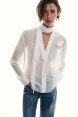 Blusa de tejido semitransparente con efecto arrugado, escote en pico y manga larga. Presenta un detalle decorativo frontal con estructura en forma de flor.